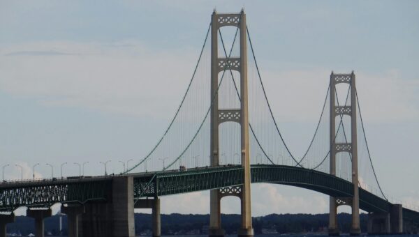 Impressive view of the Mackinac Bridge stretching across Lake Michigan under a clear blue sky, taken in St. Ignace, MI.
