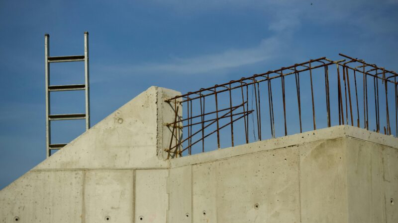 Concrete building in progress with ladder and rebar against a clear blue sky.